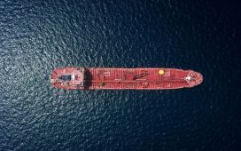 Aerial view of a red tanker ship sailing on dark blue water from above.