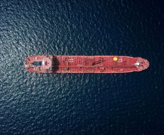 Aerial view of a red tanker ship sailing on dark blue water from above.
