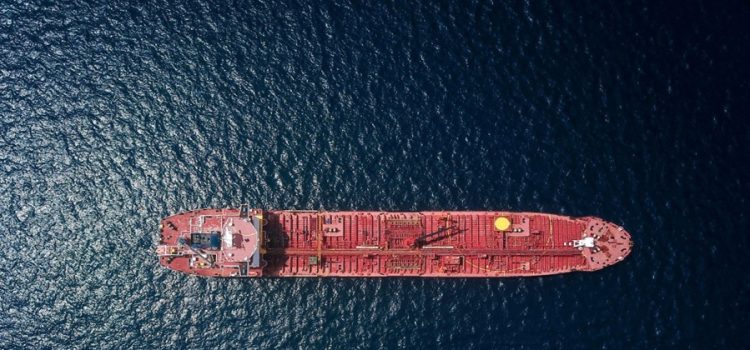 Aerial view of a red tanker ship sailing on dark blue water from above.