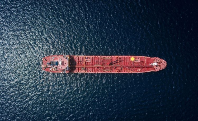 Aerial view of a red tanker ship sailing on dark blue water from above.