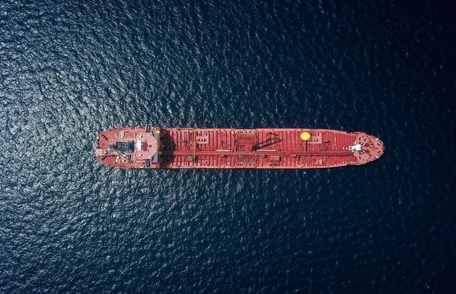 Aerial view of a red tanker ship sailing on dark blue water from above.